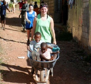 Jessica Rothstein ’13 plays with kids in Jacmel, Haiti, pushing a wheelbarrow with two boys inside.