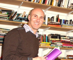 Anthony Caleshu '92 holds a book in his office, with shelves of books in the background