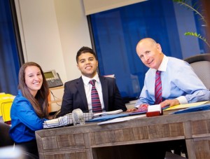 Monica Girardi ’15 and Andy Muñoz ’15 sit at a desk with Barry Bregman ’77 in his New York City office.