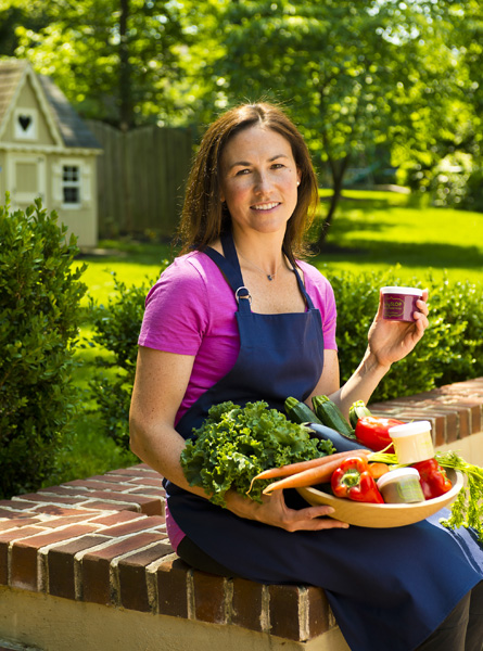 Adria Lazur Kinnier '97 sits holding a plate full of vegetables as well as a container of her baby food product