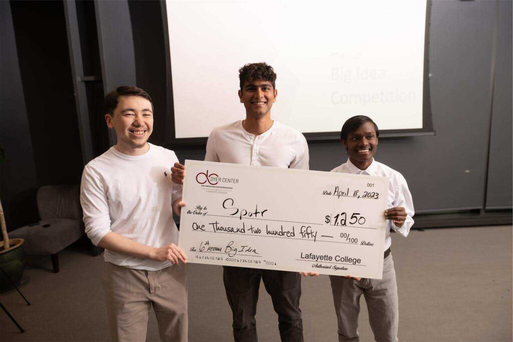 Three students smile, holding a check