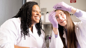 Samantha Greenberg and Khadijah Mitchell smile, holding a beaker.