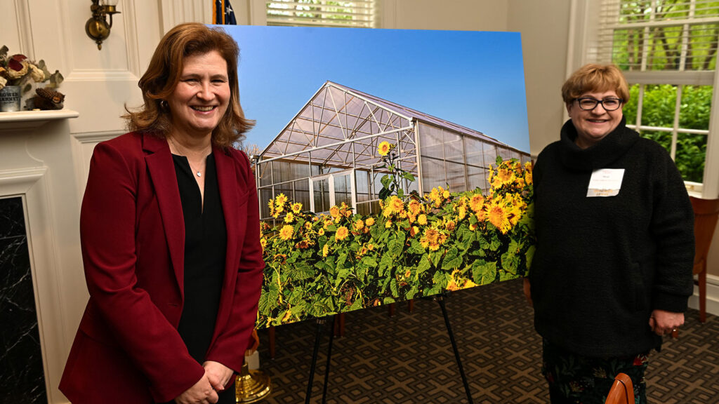 President Nicole Hurd and Heidi Ludwick Hanson '91 stand in front of a picture of the new greenhouse at Lafarm at the luncheon to dedicate the new addition to LaFarm