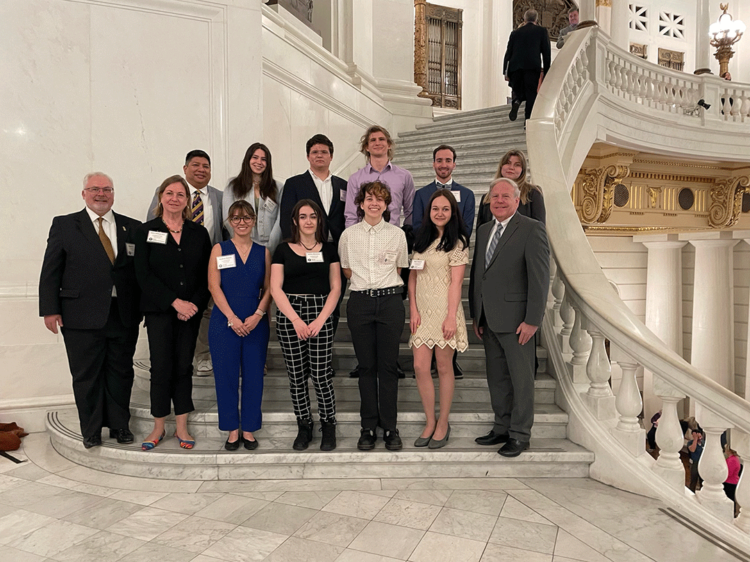 Nine students and staff members stand on stairs in the Capitol building 