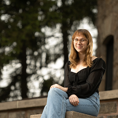 Thalia Newman smiles, sitting in a ledge outdoors.