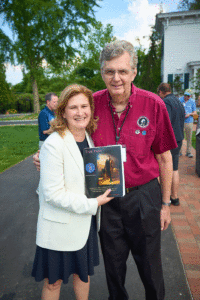 President Nicole Hurd stands with John Becica '69. Hurd is holding a book. 