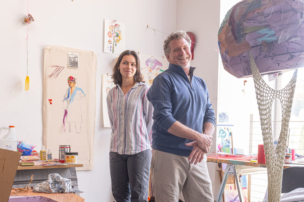 Jim Toia and Lily Dineen smile surrounded by art. 