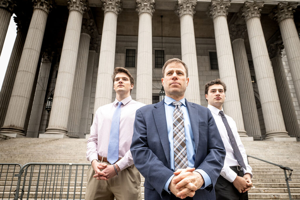 Three people stand in front of a courthouse in NYC.