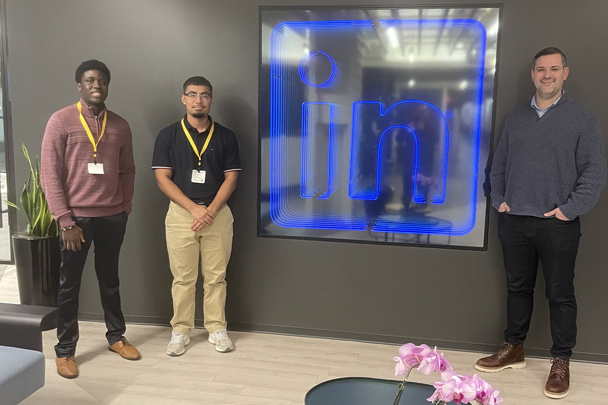 Doug Prusoff ’12, Victor Hernandez ’25 and Goodness Obadofin ’26 pose in front of a light up LinkedIn logo sign