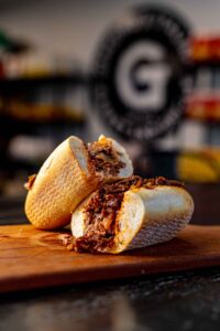 Two halves of a cheesesteak rest on a wooden board with the Giacomo's logo in the background.