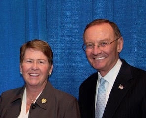 Lois and Neil Gagnon are pictured standing in front of a blue backdrop. They are both smiling and wearing lapel pins.