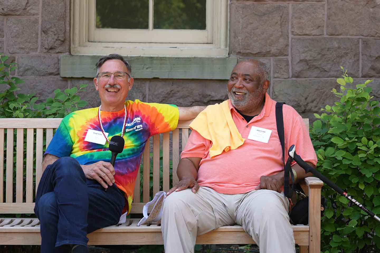 Two alumni are sitting on a bench outside of Pardee Hall.