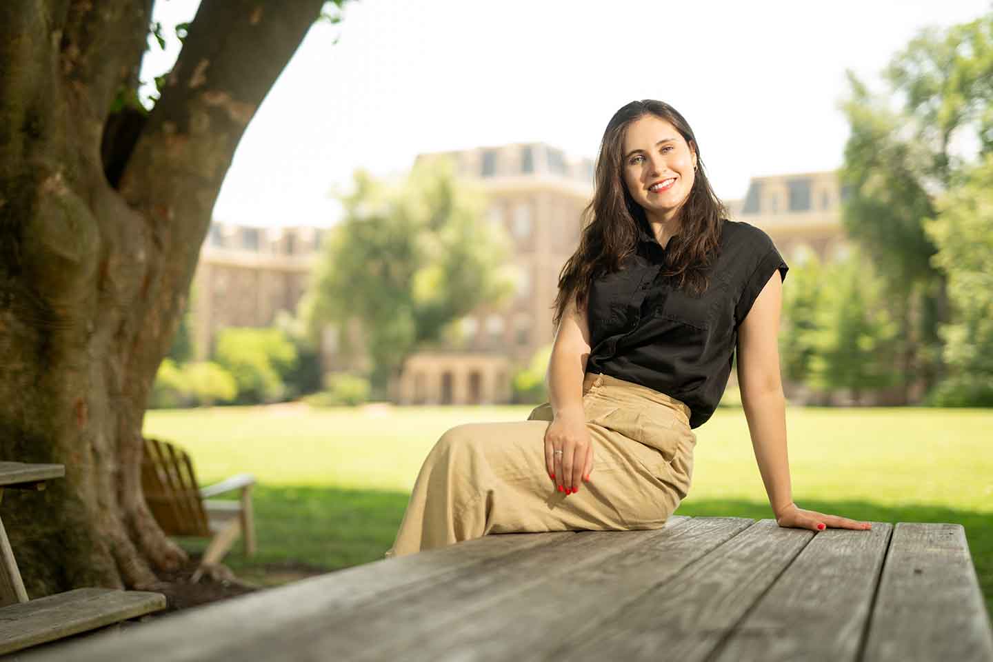 Ami Figuerrutia ’25 is sitting on a picnic table on the Quad. Pardee Hall is in the background.