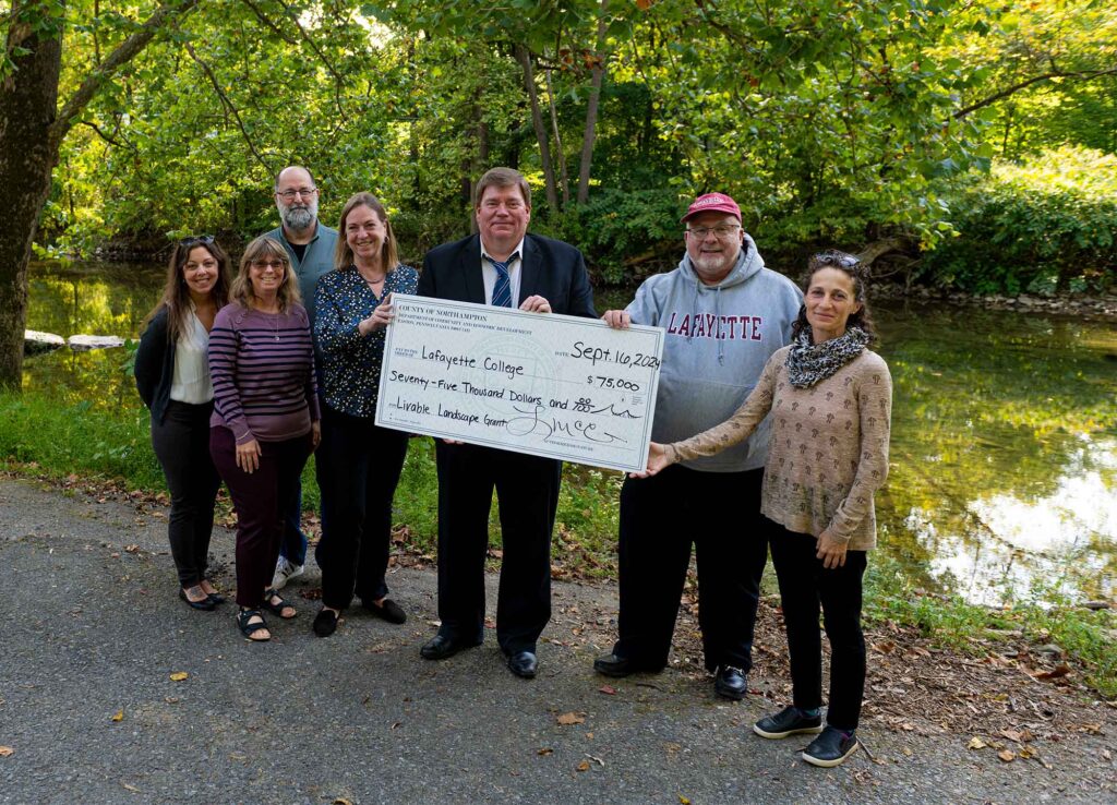 A group of seven are standing near a stream holding a large check. 