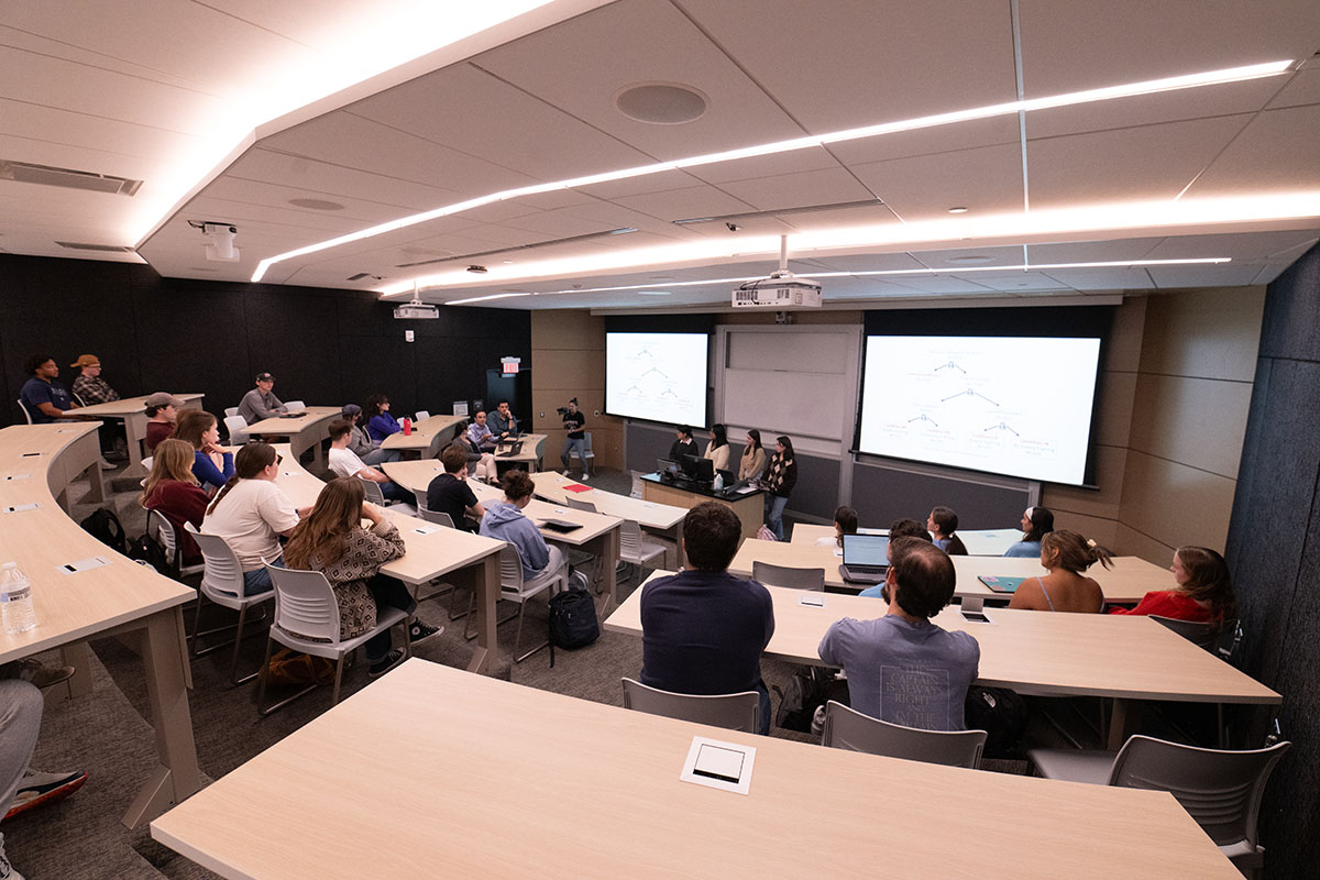 Four Gov Lab managers stand at a podium in front of a classroom full of students. 