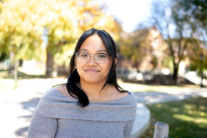 Samantha Natividad '25 smiles in front of a backdrop of trees