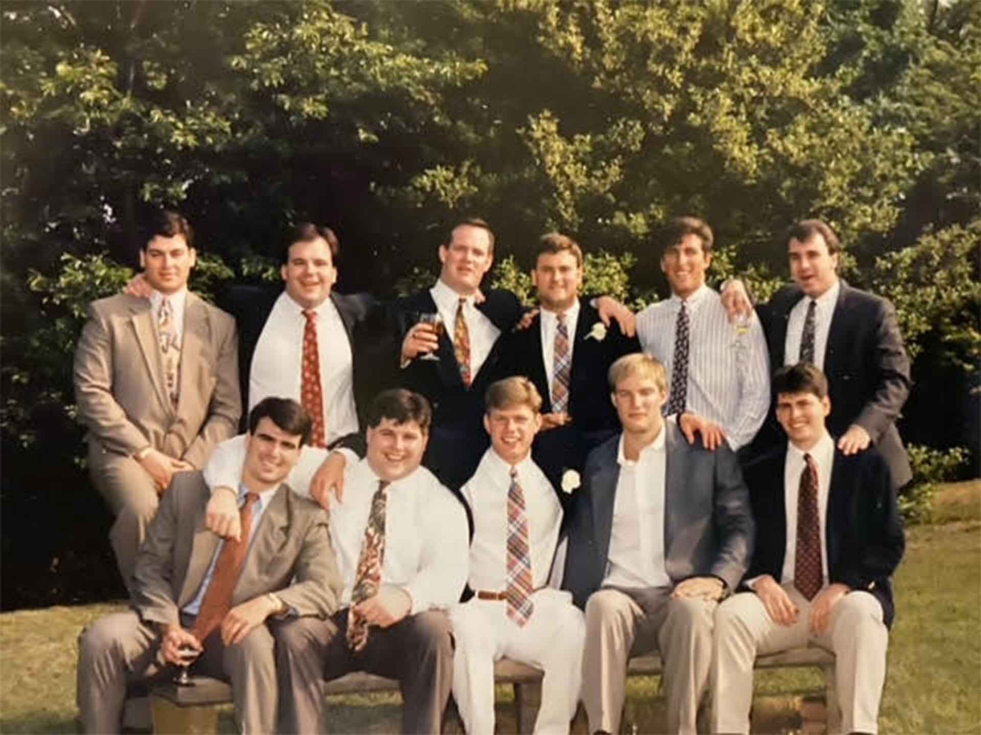 Members of the 1988 football team are posed outside. They are wearing suits. 