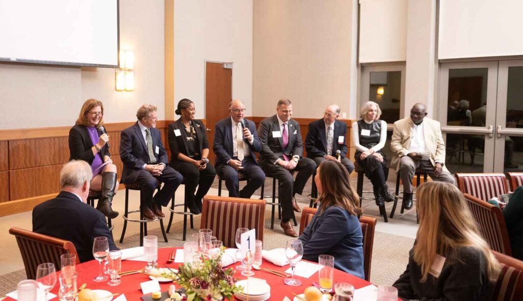 President Nicole Farmer Hurd is seated (far left) with seven members of a panel discussion. President Hurd is holding a microphone.