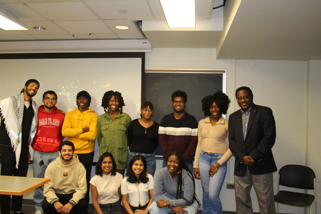 Students stand in a classroom alongside a guest speaker