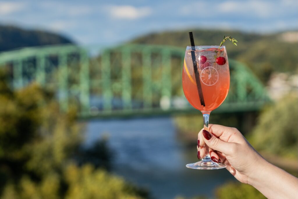 A drink glass is held at Thyme, with the background of the Delaware River and Easton Free Bridge