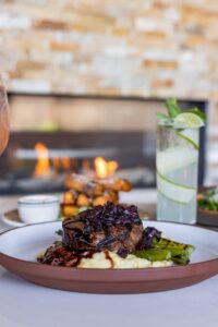 A dish of steak and asparagus with a cucumber cocktail in the background is shown on a table.