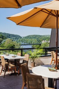 A view from Thyme Rooftop Grille's outdoor patio where yellow umbrellas cover the tables and a view of the riverside can be seen.