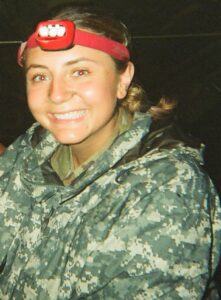 Cadet Emma Emlen '25 is pictured in her Army camouflage in the dark wearing a head lamp.