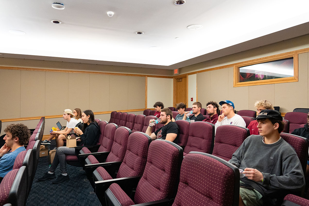 Students sit inside a theater space listening to a presentation. 