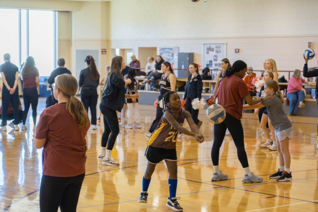 Inside the gym in Kirby Sports Center, Lafayette student-athletes work with young kids on form and technique for a variety of sports. In this photo a young girl learns to serve a volleyball