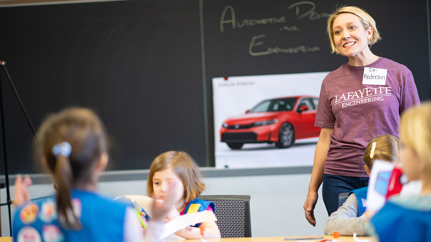 Dean of the Faculty Lauren Anderson is pictured in front of a chalkboard with an image of a car as she leads Girl Scouts through an automotive engineering session