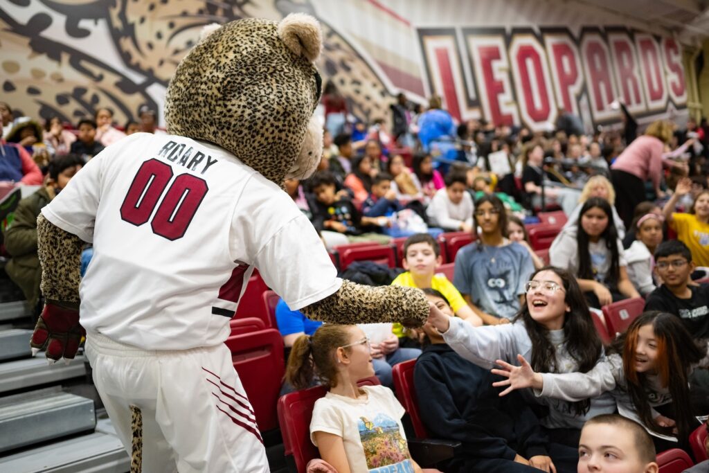 Roary the Leopard mascot high fives young fans in Kirby Sports Center during School Day Game