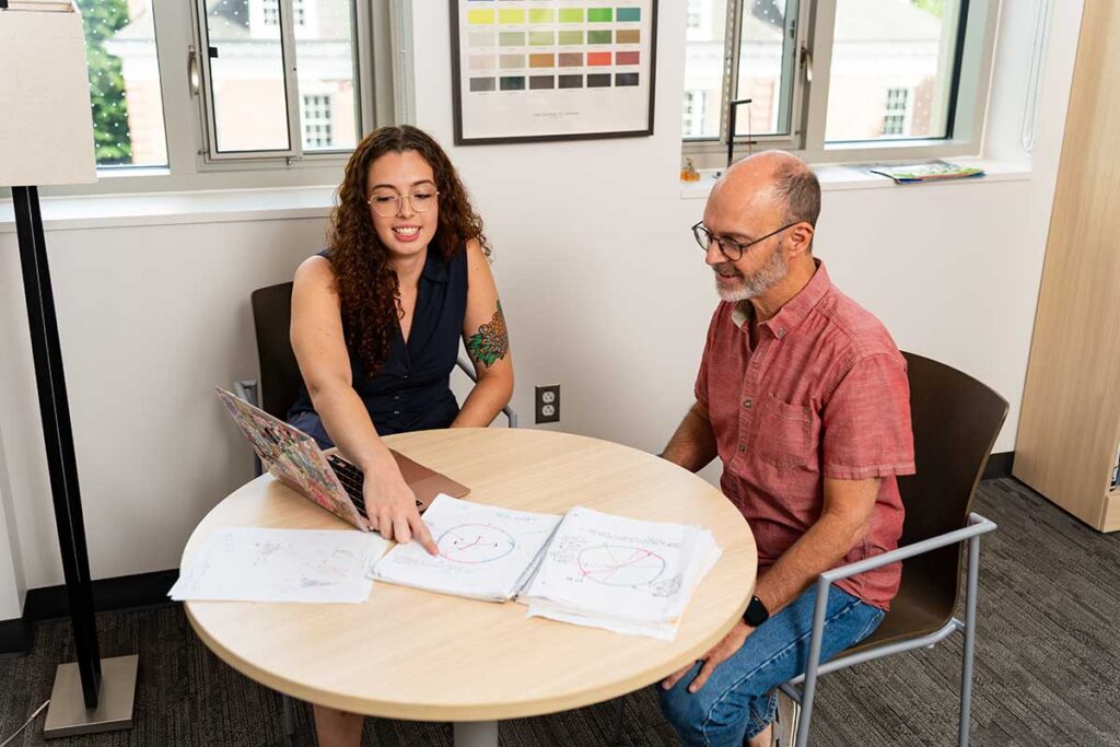 Prof. Chris Ruebeck and Mita Crane '26 sitting at a table discussing a research project impacting Ruebeck's Industrial Organization course