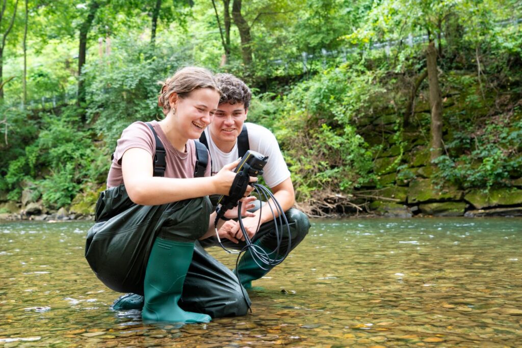 Ashley McElroy ’27 and Robbie Snyders ’26 look at an instrument while kneeling in Bushkill Creek.