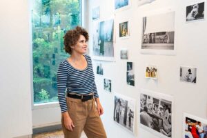 Karina Aguilera Skvirsky smiling at a display of her photos for her exhibit Viajes de los Ochentas