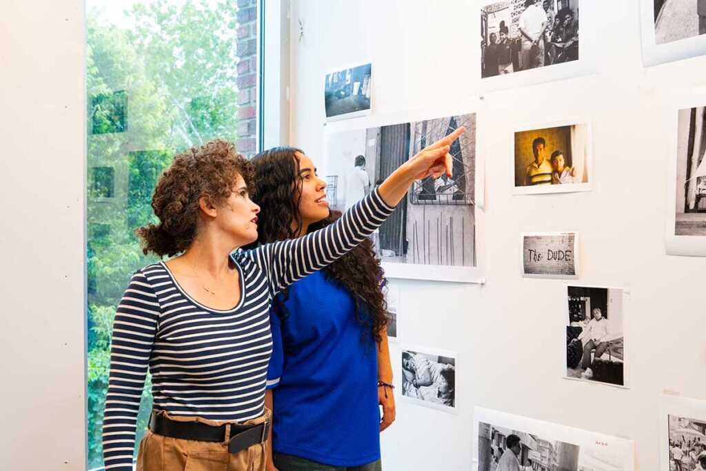 Karina Aguilera Skvirsky and Jasmin Lara '28 looking at and discussing the photos for Skvirsky's exhibit Viajes de los Ochentas