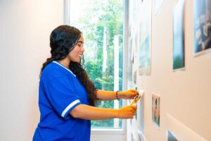 Jasmin Lara '28 adding a photo to a wall of photos collected for Karina Aguilera Skvirsky's exhibit Viajes de los Ochentas