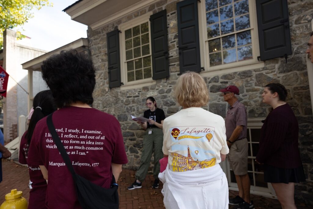 A Sigal Museum volunteer talks to a tour group in front of Bachmann Publick House. Two visitors in the foreground are wearing Lafayette Bicentennial shirts.