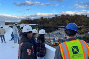 Students in Mary Wilford-Hunt's Introduction to Structural Engineering course wearing hard hats and observing from the rooftop of The Confluence during a site walk