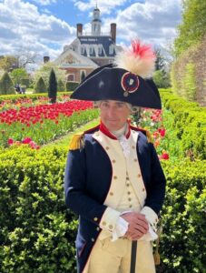 The Marquis de Lafayette poses in front of rows of flowers. 