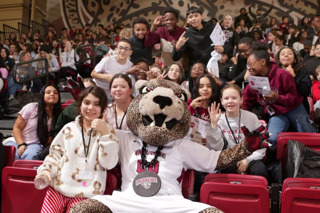 Roary the Leopard sits in the stands and poses with Easton students around him.
