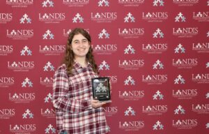 Jessica Schumer holds an award against a Landis background
