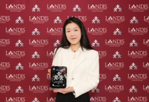 Huiyan Zou ’26 stands holding an award against a Landis logo backdrop