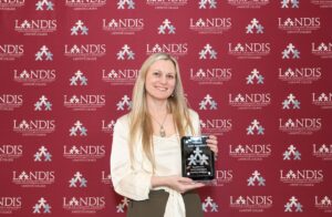 Prof. Sarah Appelhans holds a Landis Award in front of a Landis logo background