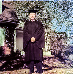 Dieu stands on the front lawn of a house in a black cap and gown