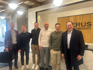 From left: Dan Cason, assistant athletic director for advancement, Digger Iqbal ’25, Colin Morissey ’20, Dennis Bohn, men’s soccer coach, Adam Decker ’03, and Brian Winiarski ’86 stand and smile at the camera at the office of Merus in New York City.