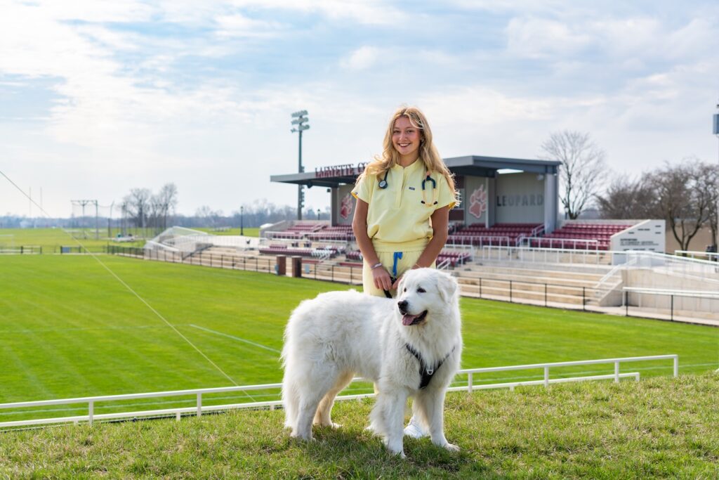 Ashley Martinho '26 is pictured in scrubs with a fluffy dog standing in front of Gummeson Grounds