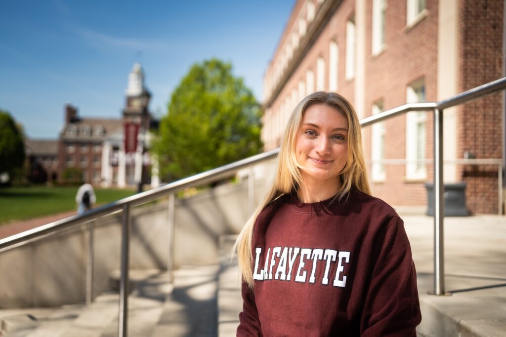 Grace Trautwein wears a Lafayette sweatshirt as she sits on the steps of Acopian with Watson Hall in the background.