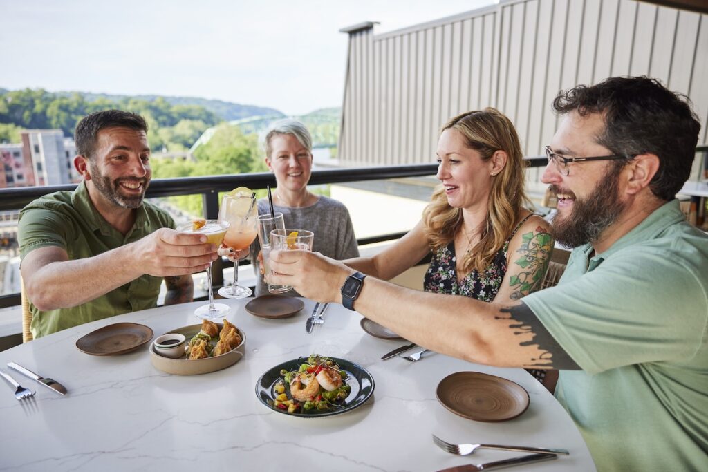 Four diners clink glasses in a toast at the rooftop dining area at Thyme.