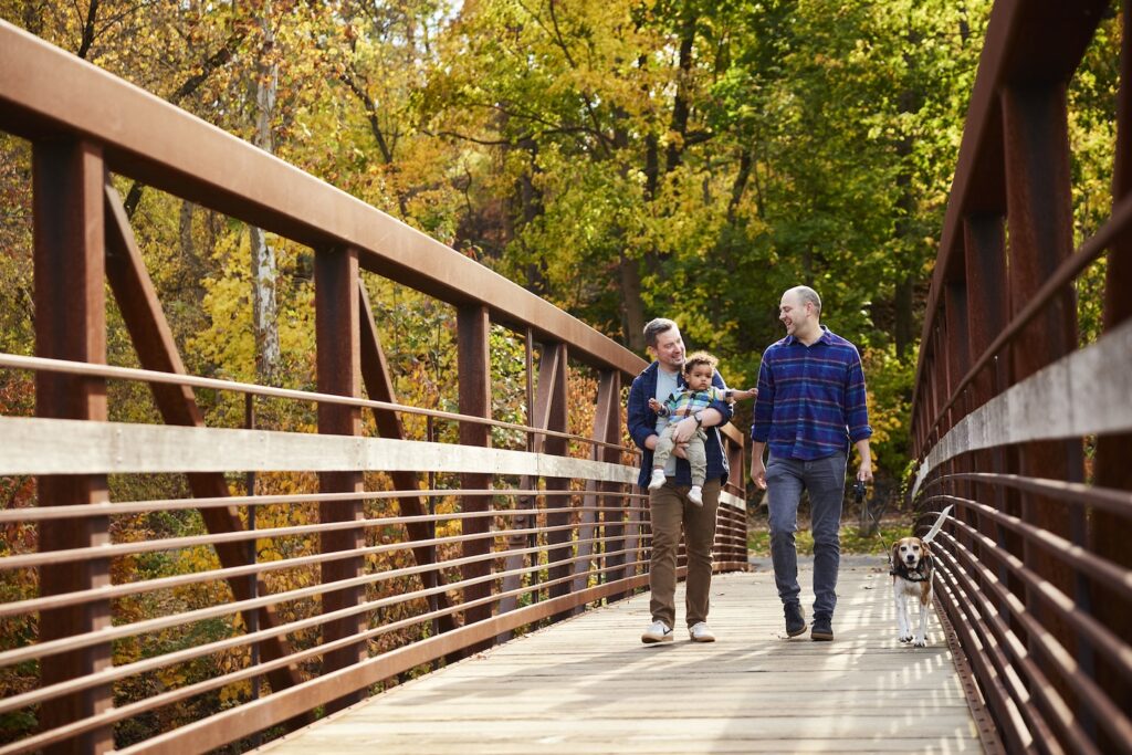 Two men and a baby walk across the bridge at Karl Stirner Arts Trail.