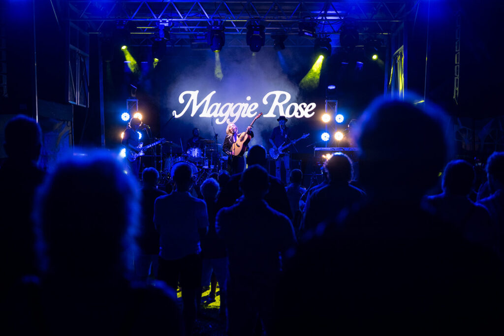 Wide shot of the a stage. Maggie Rose is on a sign in the background. 